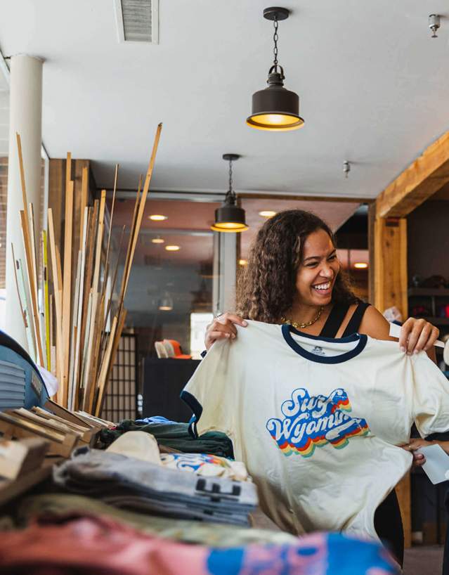 Shoppers holding up Wyoming shirt in store featuring clothing and outdoor-themed merchandise.