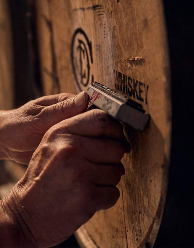 Wood barrel being stamped WHISKEY by pair of hands.