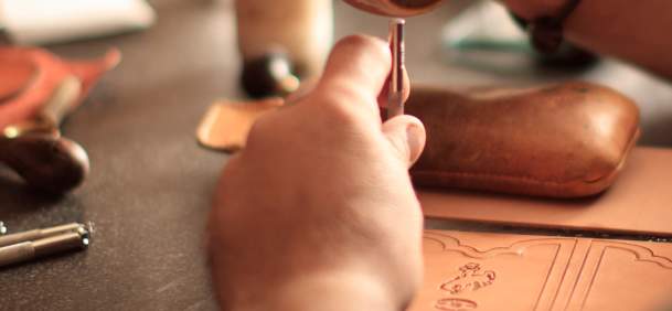 Hands crafting leather with tools.